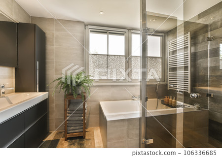 a modern bathroom with a tub, sink and toilet in the background is a plant on the side of the bathtub a modern bathroom with a tub, sink and toilet in the background is a plant on the side of the bathtub 106336685