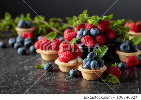 Small tartlets with fresh raspberries and blueberries on a black background. Small tartlets with fresh raspberries and blueberries on a black background. 106340324