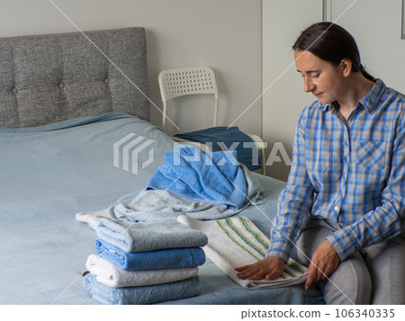 Woman folding clean terry towel in the bedroom. Organizing laundry at home. Woman folding clean terry towel in the bedroom. Organizing laundry at home. 106340335
