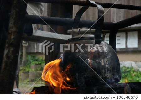 Heating a kettle over a bonfire while camping 106340670