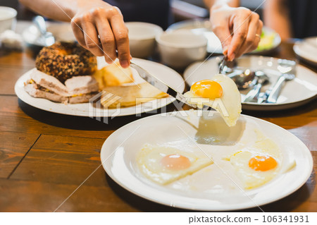Woman eating fried eggs breakfast with friends on wooden table. Woman eating fried eggs breakfast with friends on wooden table. 106341931