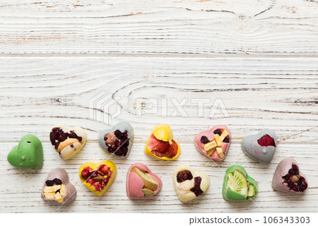 chocolate sweets in the form of a heart with fruits and nuts on a colored background. top view with space for text, holiday concept chocolate sweets in the form of a heart with fruits and nuts on a colored background. top view with space for text, holiday concept 106343303