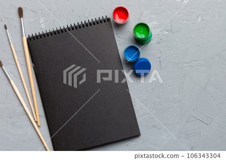 Album pages and paints, pencils, brush on a colored background. Top view with empty space. workplace for creativity. home teaching concept drawing Album pages and paints, pencils, brush on a colored background. Top view with empty space. workplace for creativity. home teaching concept drawing 106343304