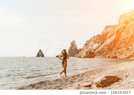 Woman travel summer sea. A happy tourist in a blue bikini enjoying the scenic view of the sea and volcanic mountains while taking pictures to capture the memories of her travel adventure. Woman travel summer sea. A happy tourist in a blue bikini enjoying the scenic view of the sea and volcanic mountains while taking pictures to capture the memories of her travel adventure. 106343957