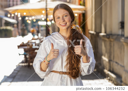 Happy girl showing thumbs up, like sign positive something good positive feedback in city street 106344232