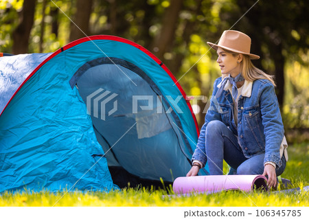 Young blonde woman stending near the tent with a mat in hands Young blonde woman stending near the tent with a mat in hands 106345785