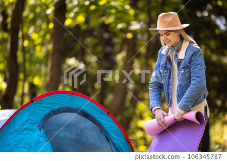 Young blonde woman stending near the tent with a mat in hands Young blonde woman stending near the tent with a mat in hands 106345787