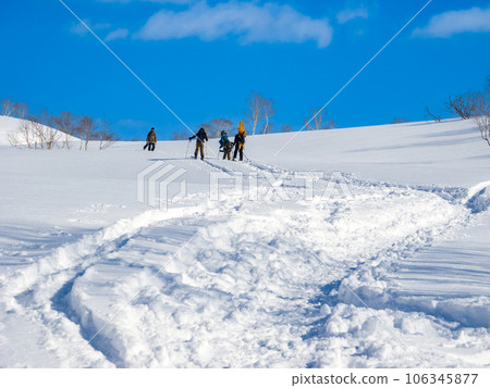 People walking on a snowy field with snowboards on their backs (Hokkaido, around the Iwaonupuri trailhead) 106345877
