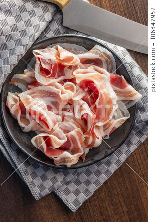 Italian panchetta. Sliced smoked bacon on plate. Top view. 106347952