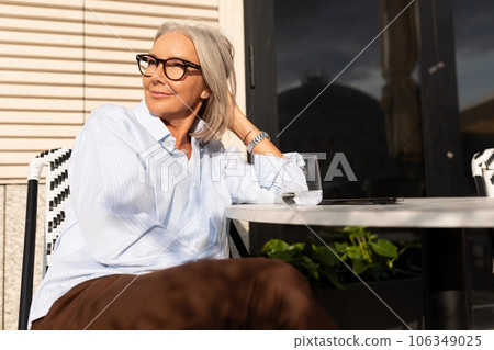 portrait of a slender gray-haired middle-aged business woman dressed in a shirt sitting in a cafe 106349025