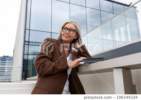 a slender senior business woman with gray hair and glasses dressed in a jacket is waiting for a 106349184