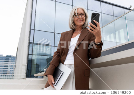 happy mature old woman with gray hair and glasses is dressed in a stylish jacket goes to a business 106349200