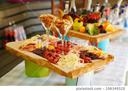 A wooden tray with cheese and meat appetizers on the banquet table. A wooden tray with cheese and meat appetizers on the banquet table. 106349320