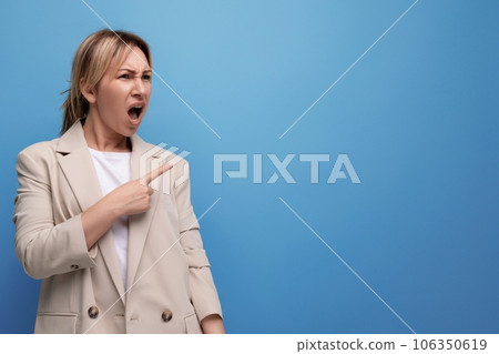 surprised blond young woman in jacket pointing finger to side on studio background 106350619