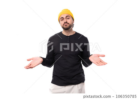 a handsome young 30 year old guy with a beard dressed in a black jacket and a yellow hat shrugs his a handsome young 30 year old guy with a beard dressed in a black jacket and a yellow hat shrugs his 106350785