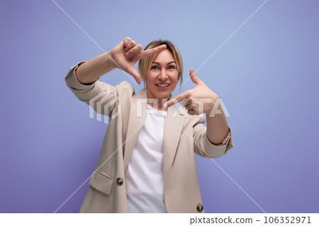 cheerful woman in a jacket with blond hair makes a photo with the help of her hands on a studio cheerful woman in a jacket with blond hair makes a photo with the help of her hands on a studio 106352971