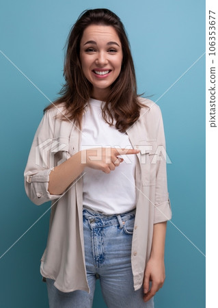 funny european young brunette woman in shirt and jeans pointing finger to the side on blue funny european young brunette woman in shirt and jeans pointing finger to the side on blue 106353677