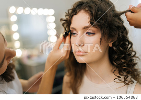 Close-up face of sensual woman getting applying mascara on eyelashes from makeup artist in beauty salon. Professional female hairdresser giving beauty salon service and treatment to beautiful customer Close-up face of sensual woman getting applying mascara on eyelashes from makeup artist in beauty salon. Professional female hairdresser giving beauty salon service and treatment to beautiful customer 106354868