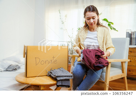 volunteer asian woman putting unused clothes into cardboard boxes for donation and charity. Reuse, recycle, renewable and sustainability concept. 106356247