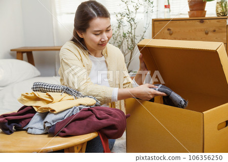 Young asian female putting clothes into cardboard box to moving to new house or apartment. 106356250