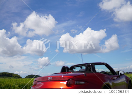 Driving in a red open car through the countryside and the blue sky with clouds floating in it 106356284