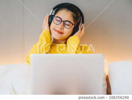 Asian woman enjoying listening music in headphones while quarantine herself at home. Conceptual of woman lifestyle. Asian woman enjoying listening music in headphones while quarantine herself at home. Conceptual of woman lifestyle. 106356290