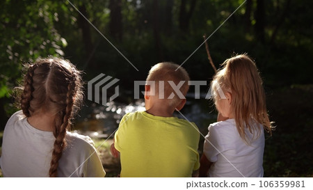 children sit on the banks of the river. happy family childhood dream concept. a group lifestyle of little children sit together by the river and talk. kids spend time outdoors in nature in the forest children sit on the banks of the river. happy family childhood dream concept. a group lifestyle of little children sit together by the river and talk. kids spend time outdoors in nature in the forest 106359981