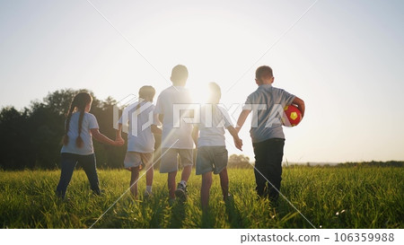 a group of children walk on the grass in the park with a ball. happy family childhood dream concept. little children walk around the meadow with green grass and holding hands together lifestyle 106359988
