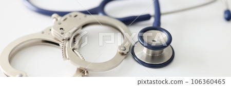 An handcuffs and a blue stethoscope on a white background An handcuffs and a blue stethoscope on a white background 106360465