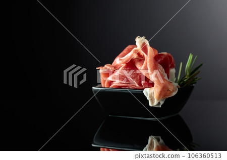 Prosciutto with rosemary on a black background. Prosciutto with rosemary on a black background. 106360513