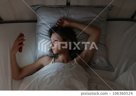 Sleepy female watching her smartphone in bed at night. Sleepy female watching her smartphone in bed at night. 106360524