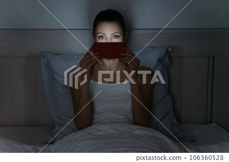 Young woman laying in bed late at night and holding smartphone in her hands. Young woman laying in bed late at night and holding smartphone in her hands. 106360528