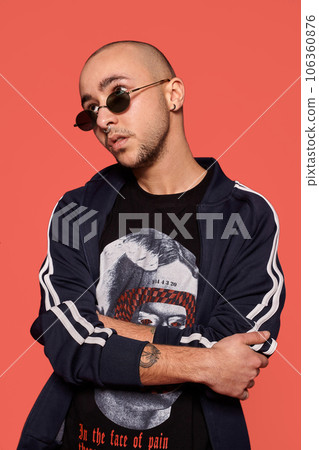 Studio shot of a young tattoed bald man posing against a pink background. 90s style. Studio shot of a young tattoed bald man posing against a pink background. 90s style. 106360876