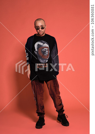 Studio shot of a young tattoed bald man posing against a pink background. 90s style. Studio shot of a young tattoed bald man posing against a pink background. 90s style. 106360881