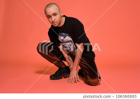 Studio shot of a young tattoed bald man posing against a pink background. 90s style. 106360883
