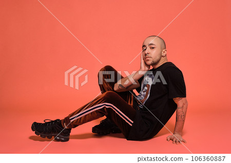 Studio shot of a young tattoed bald man posing against a pink background. 90s style. Studio shot of a young tattoed bald man posing against a pink background. 90s style. 106360887