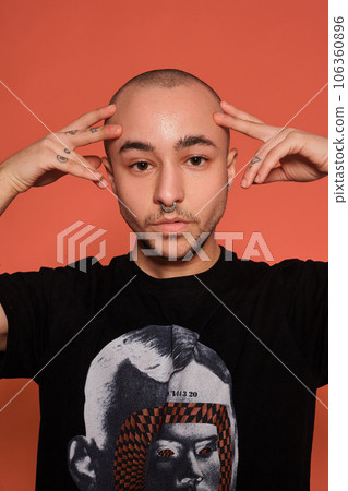 Studio shot of a young tattoed bald man posing against a pink background. 90s style. 106360896