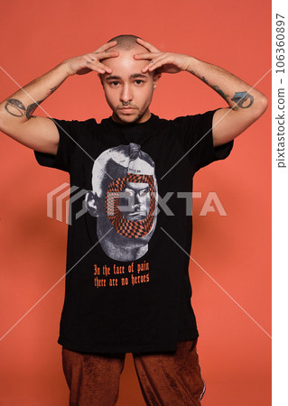 Studio shot of a young tattoed bald man posing against a pink background. 90s style. Studio shot of a young tattoed bald man posing against a pink background. 90s style. 106360897