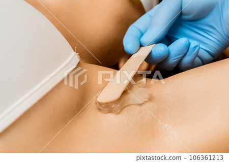 Professional smears transparent wax on lady client armpit area. Hair removal and spa services. Smearing stretchy structure on woman body part 106361213