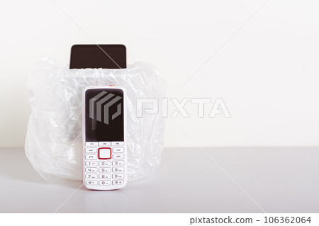 A white push-button telephone stands by the trash can with a smartphone on the table A white push-button telephone stands by the trash can with a smartphone on the table 106362064