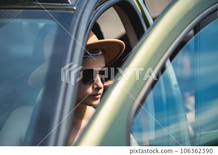 Portrait of a serious young woman in a safari hat and sunglasses driving a car Portrait of a serious young woman in a safari hat and sunglasses driving a car 106362390