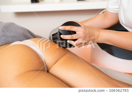 Modern electric massager with usage to correct body shape in clinic. Professional massage master works with clients legs with vibrotherapy machine 106362765