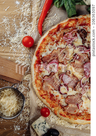 Pizza with chicken cheese and pepperoni, a piece of which is cut and laid out like a pakman, is on a wooden board and a brown background. Cheese spreads flowing streaks 106363097