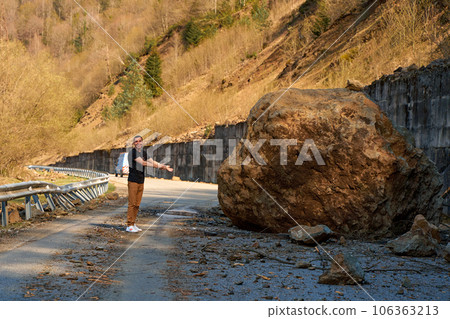 A huge rock fell from the mountains onto the road, destroying the asphalt and blocking half of the roadway 106363213
