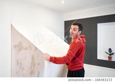 Repair the house with their own hands. The guy is ripping the old wallpaper off the wall 106363215