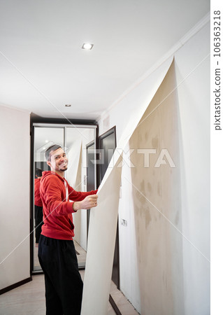 Repair the house with their own hands. The guy is ripping the old wallpaper off the wall 106363218