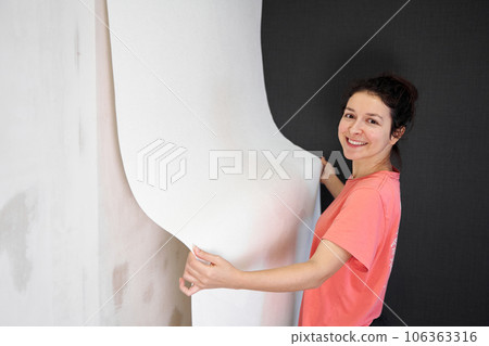 Repair and renovate the interior of the house with their own hands. The girl is tearing off the old wallpaper from the wall 106363316