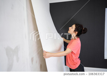 Repair and renovate the interior of the house with their own hands. The girl is tearing off the old wallpaper from the wall 106363317