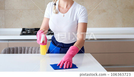 Cleaning home table sanitizing kitchen table surface with disinfectant spray bottle washing surfaces with towel and gloves. COVID-19 prevention sanitizing inside. 106363723