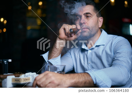 portrait of hansome man smoking cigar in a lounge bar portrait of hansome man smoking cigar in a lounge bar 106364180